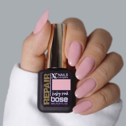 Main tenant la Base Repair Baby Pink de Nails Company, teinte rose douce visible sur la plaque naturelle