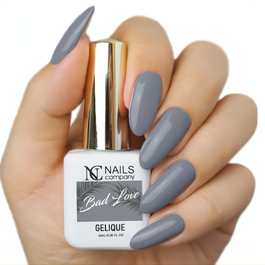 Main tenant le flacon de vernis semi-permanent Bad Love de Nails Company, gris profond visible sur ongles naturels