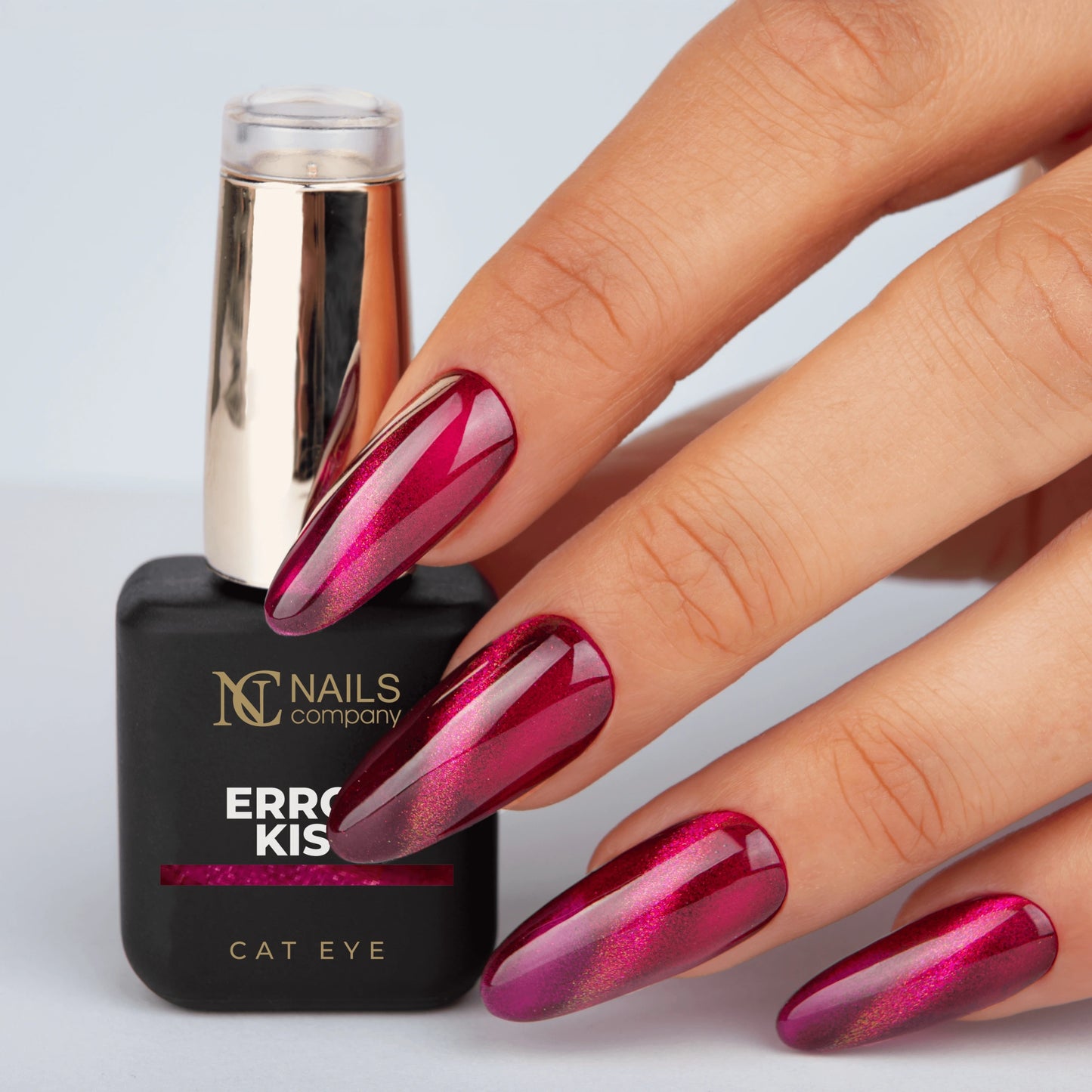 Main tenant le flacon de vernis semi-permanent Error Kiss de Nails Company, rouge violacé cat eye visible sur l’ongle