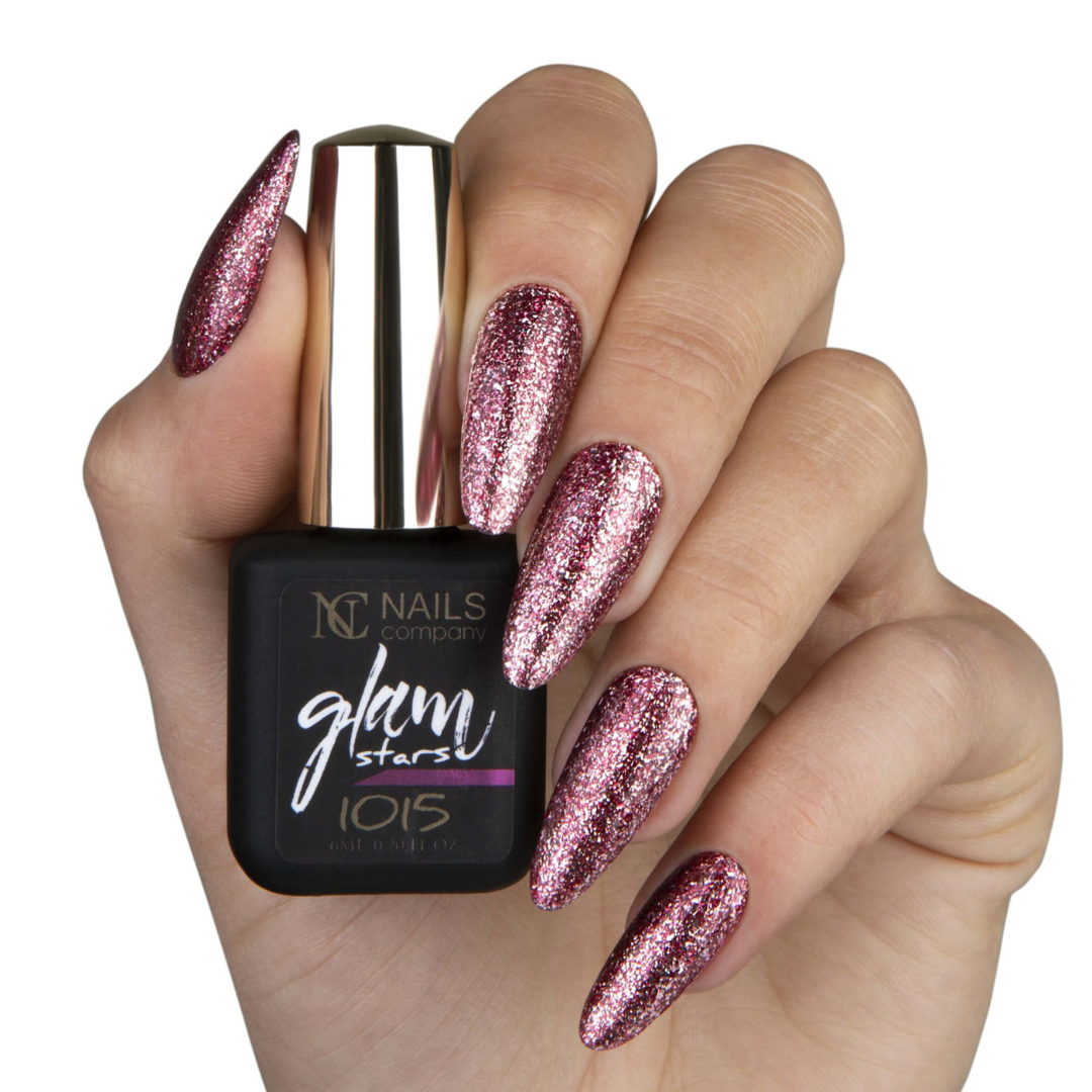 Main tenant le flacon de vernis semi-permanent Glam Stars 1015 de Nails Company, rouge foncé pailleté visible sur les ongles