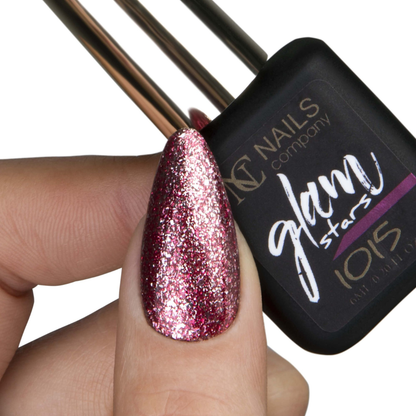 Main tenant le flacon de vernis semi-permanent Glam Stars 1015 de Nails Company, pouce avec paillettes rouges visibles