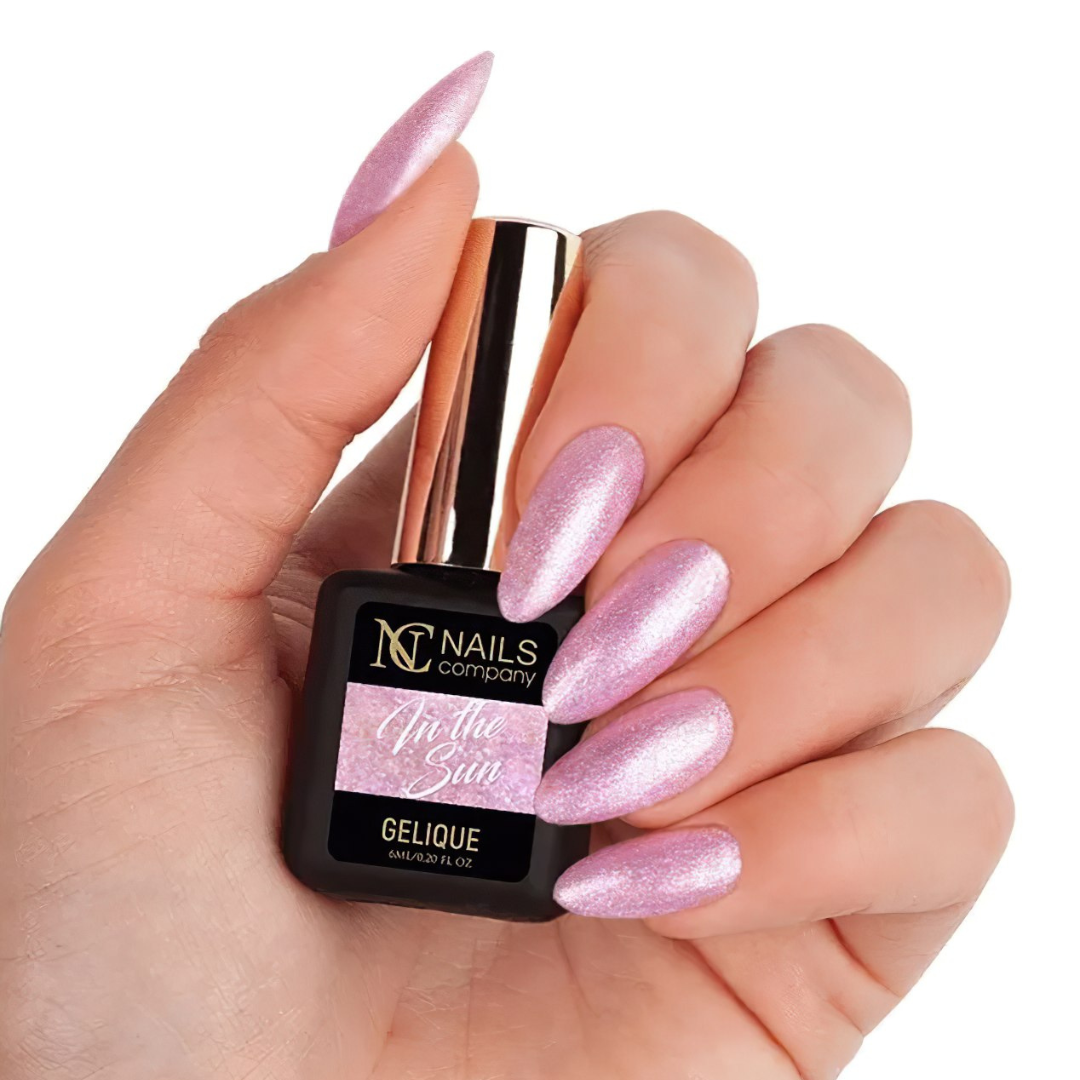 Main tenant le flacon de vernis semi-permanent In the Sun de Nails Company, rose pailleté visible sur ongles