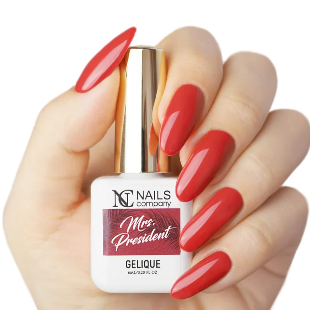 Main tenant le flacon de vernis semi-permanent Mrs. President de Nails Company, rouge soutenu visible sur ongles naturels