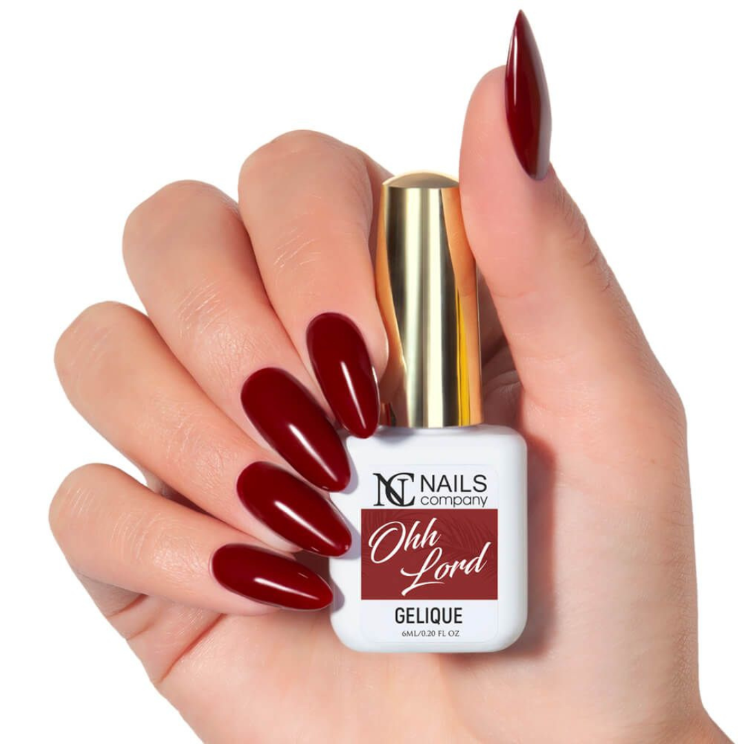 Main tenant le flacon de vernis semi-permanent Ohh Lord de Nails Company, rouge foncé bordeaux visible sur ongles