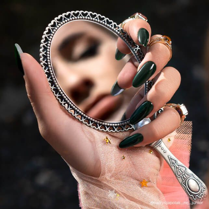 Main avec ongles en vernis semi-permanent Onyx Green de Nails Company, vert foncé présenté en tenant un miroir