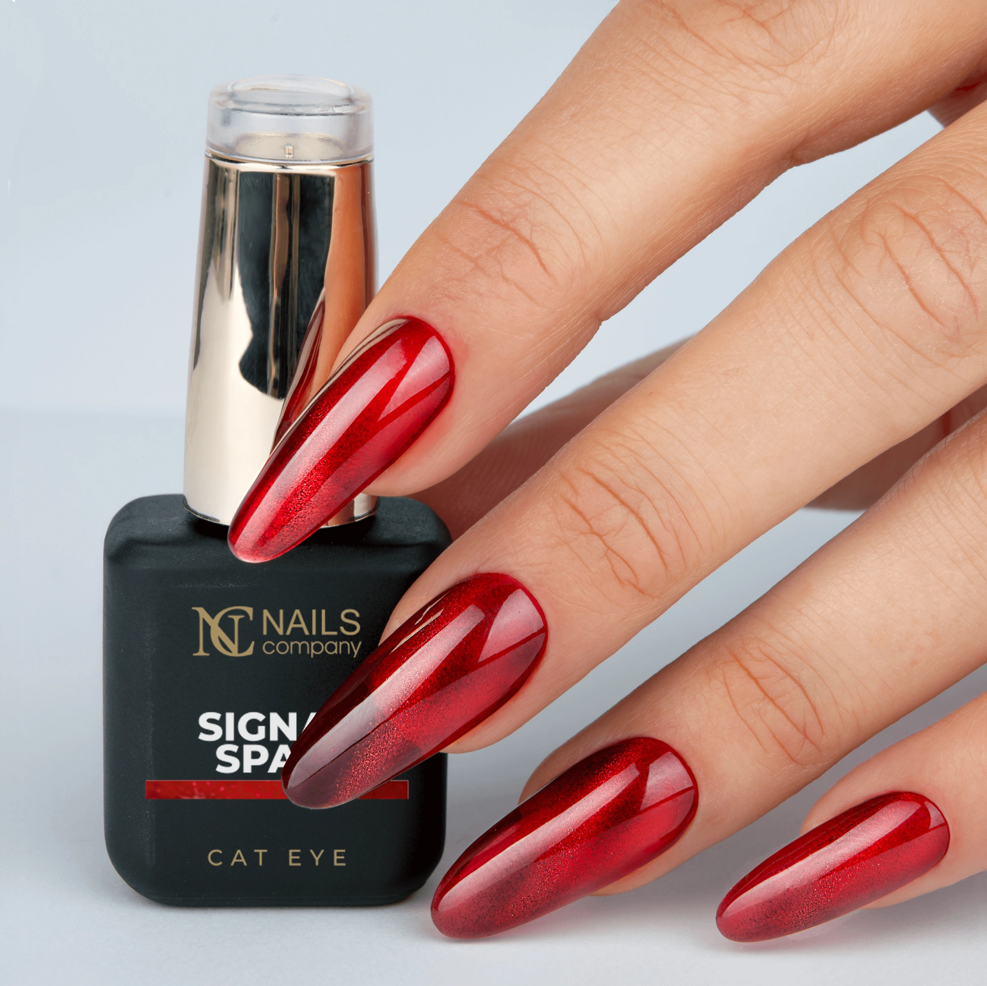 Main tenant le flacon de vernis semi-permanent Signal Spam de Nails Company, rouge orangé cat eye visible sur l’ongle
