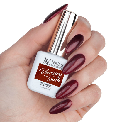 Main tenant le flacon de vernis semi-permanent Uprising Touch de Nails Company, rouge bordeaux à particules sur base sombre